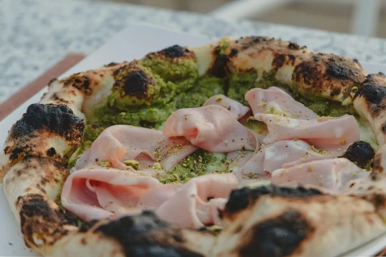 A pesto-based pizza topped with folded slices of cured ham and stracciatella