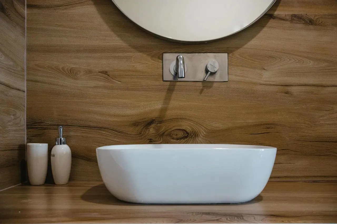 A bathroom vanity in figured timber with a round mirror and a vessel basin